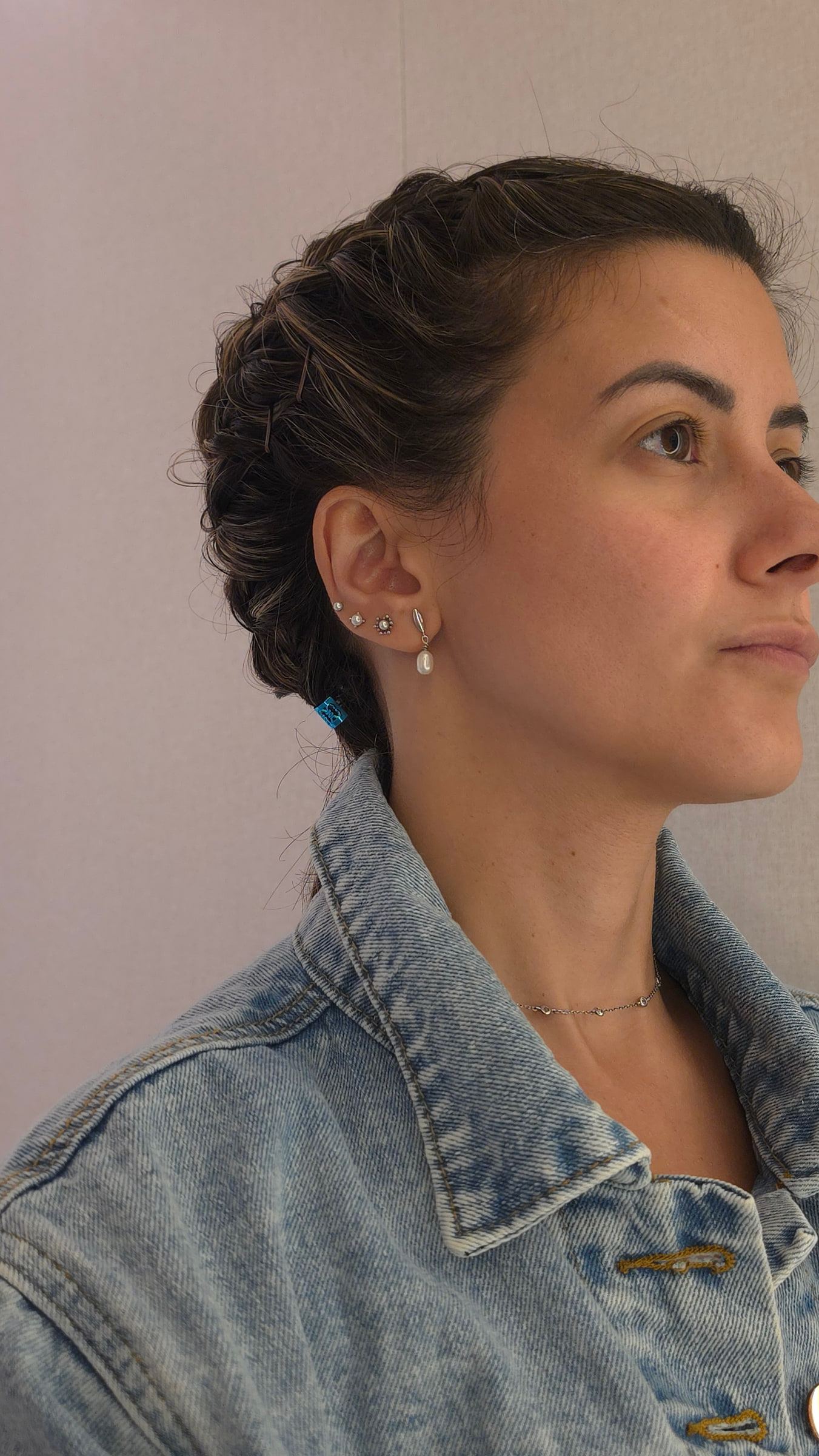 Perfil de una mujer con trenza y cazadora vaquera clara contra una pared lisa.