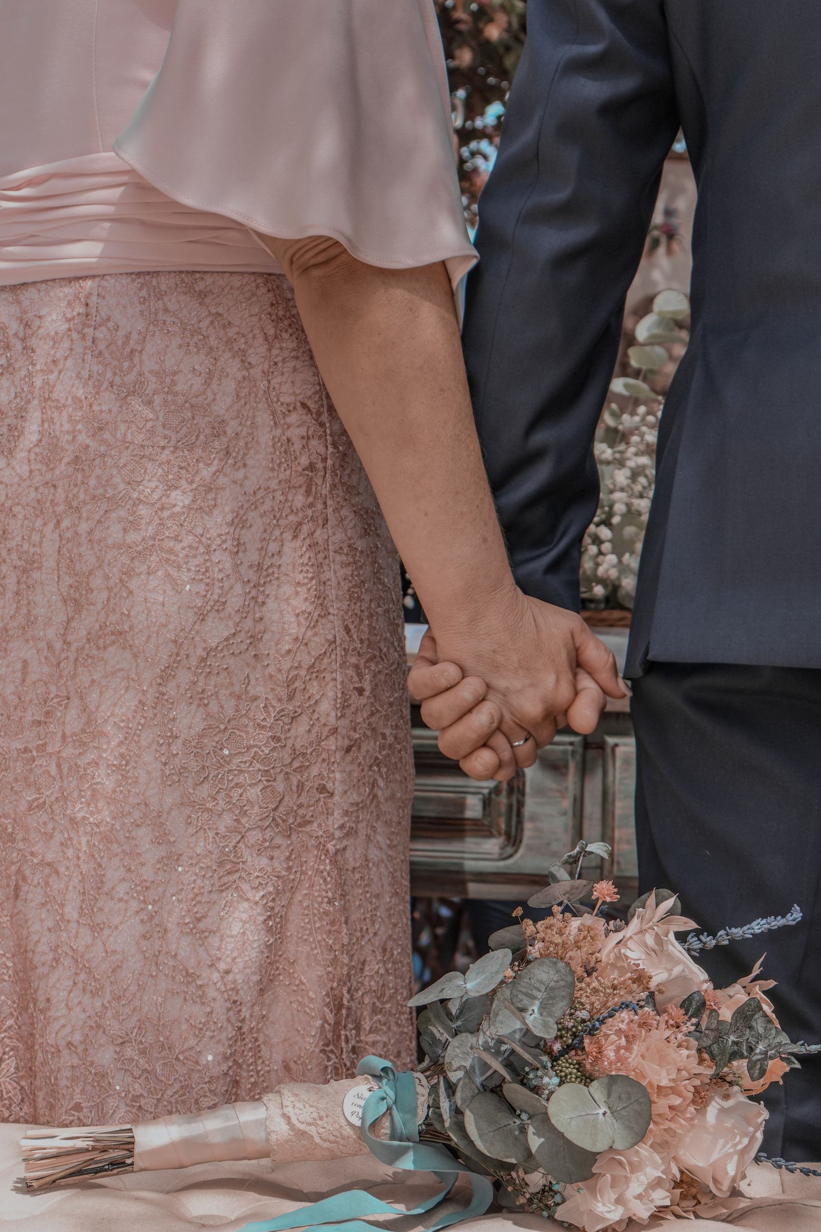 Detalle de una pareja cogida de la mano, con el ramo de flores secas y eucalipto apoyado delante.