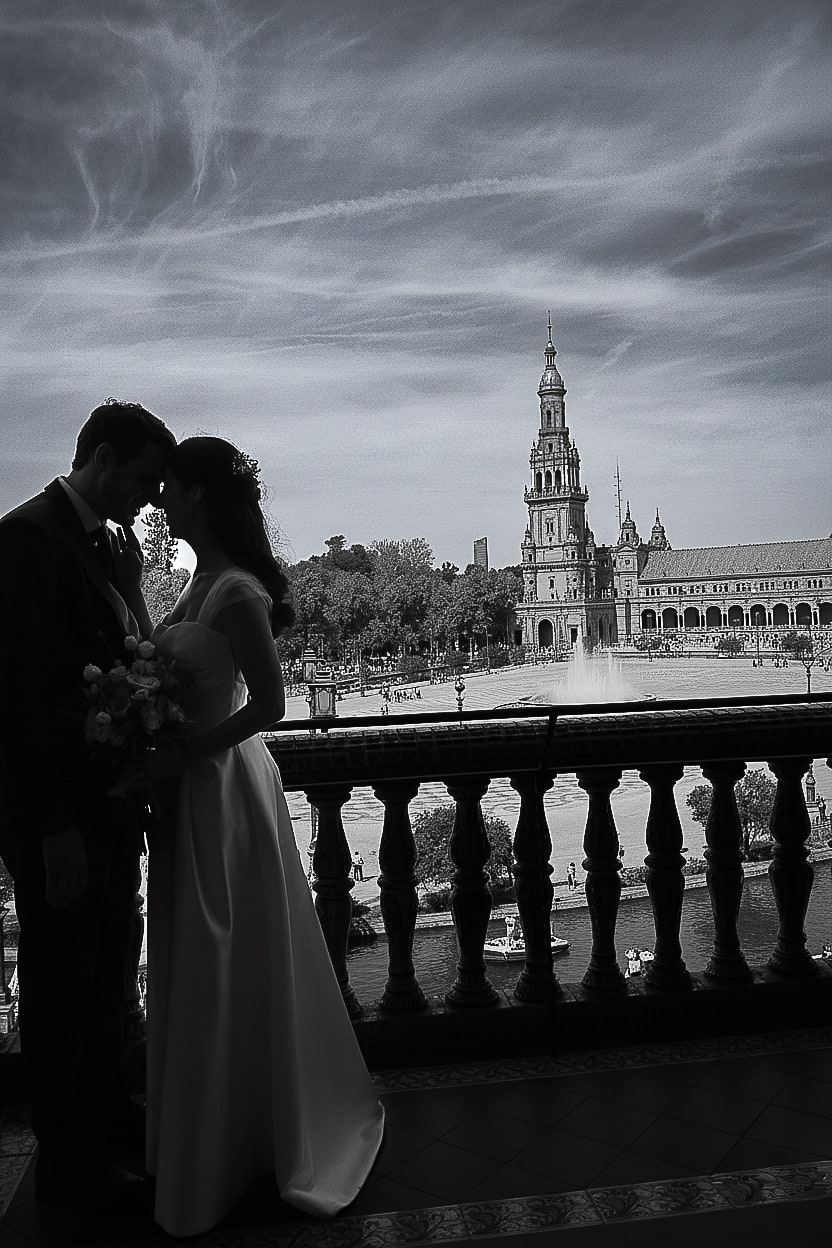 Blanco y negro: silueta de los novios frente con frente en una balconada, con la Plaza de España al fondo.