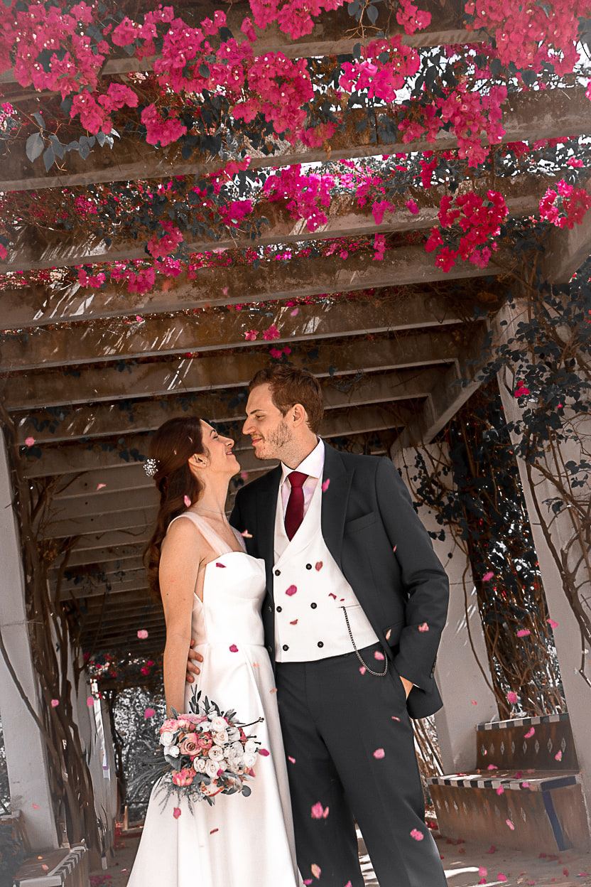 Los novios se miran bajo una pérgola cubierta de buganvilla fucsia.