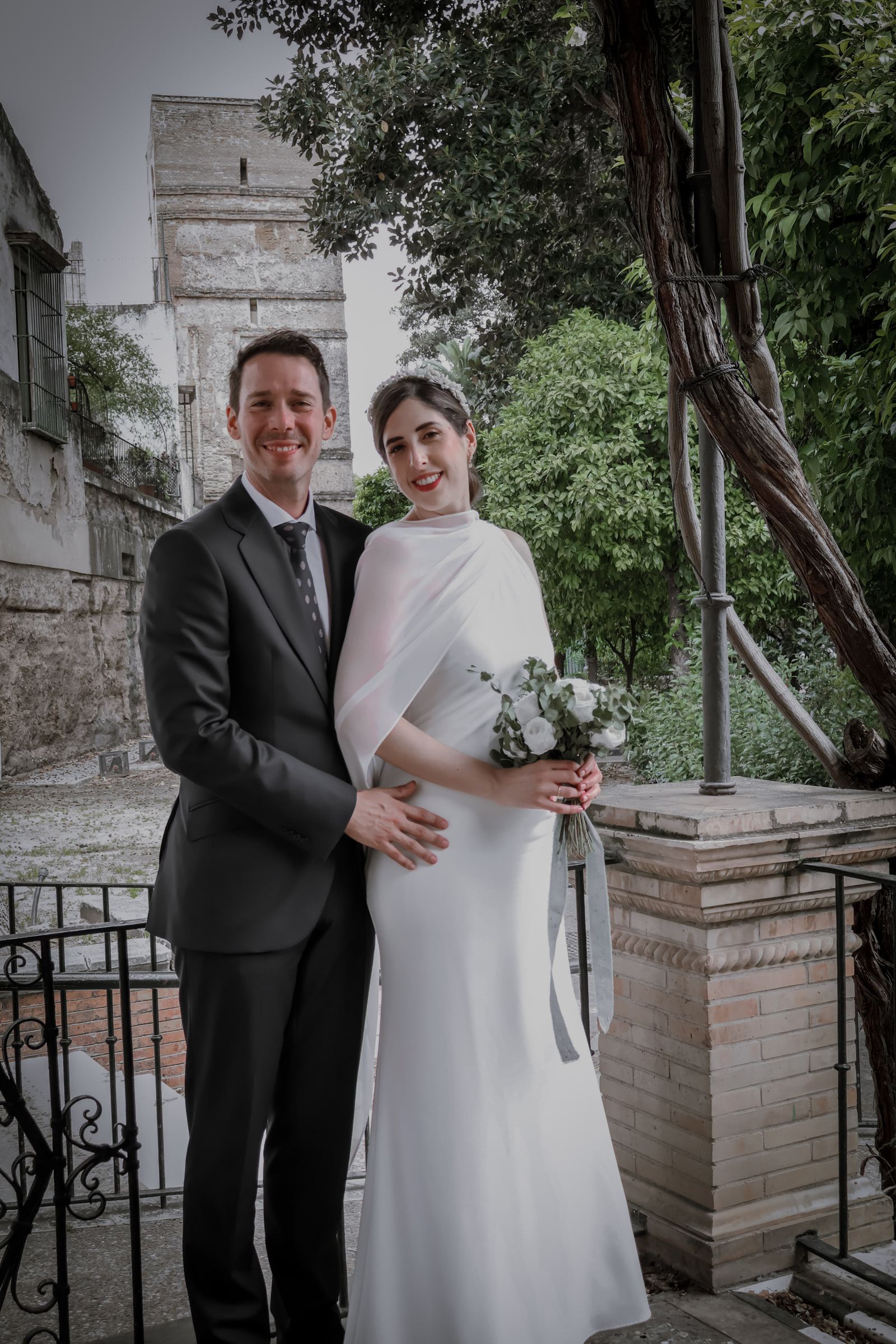 Retrato de los novios en un jardín con una torre almenada al fondo.