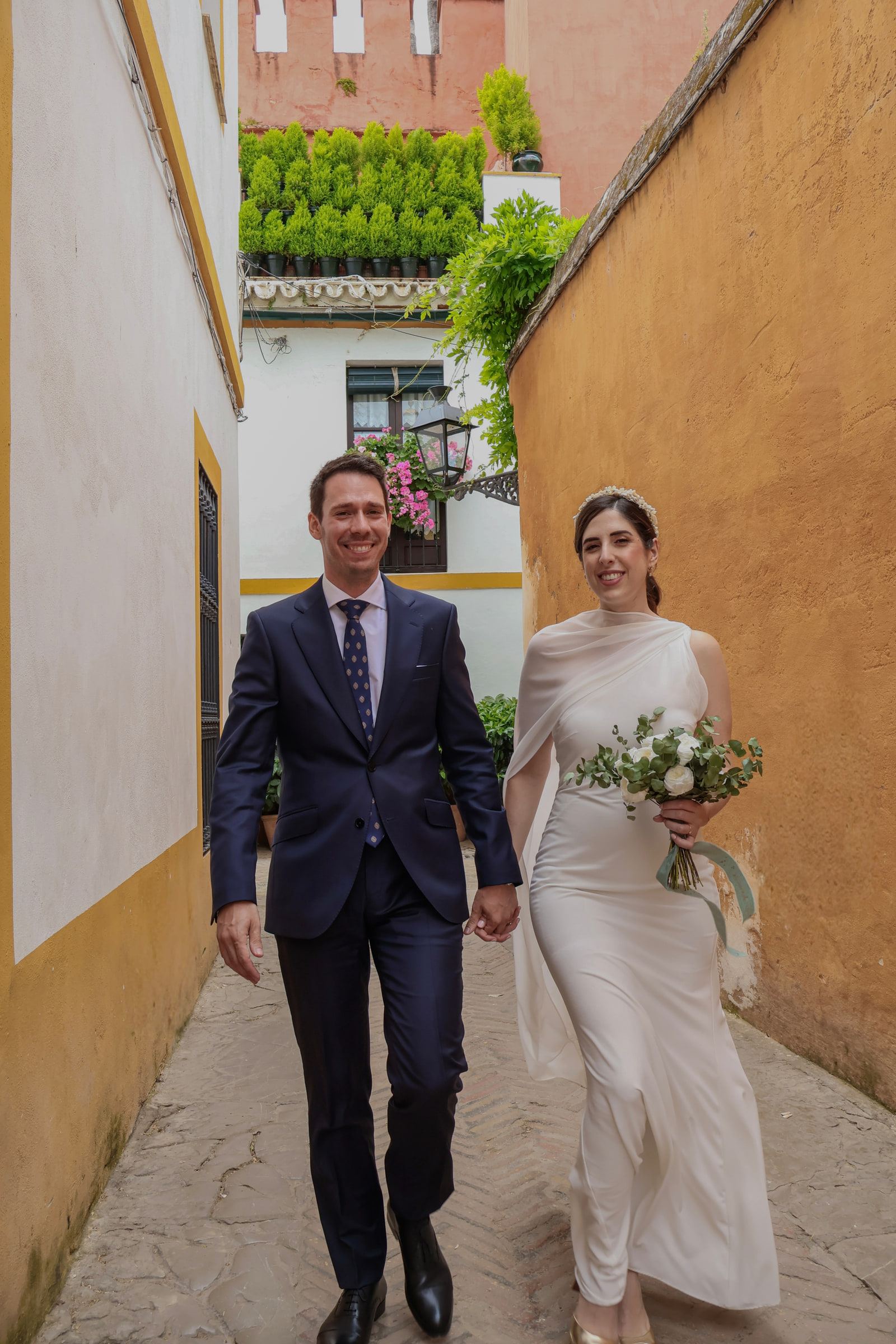 Los novios caminan de la mano por un callejón de paredes albero y blancas del barrio de Santa Cruz.