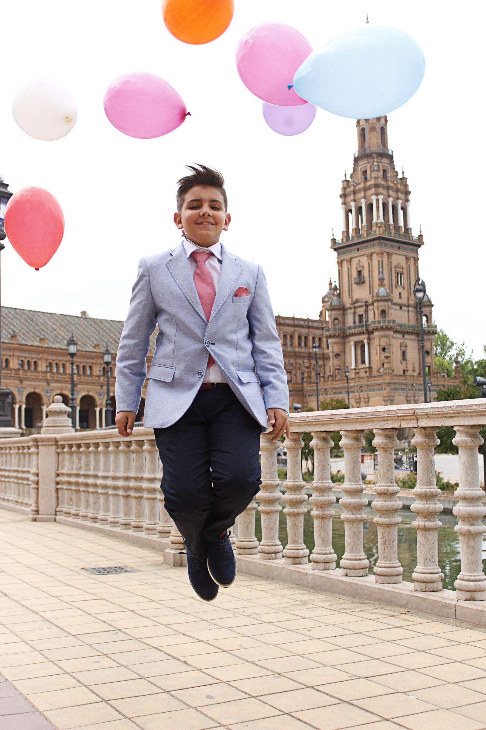 Un niño de comunión salta en el puente de la Plaza de España mientras se le escapan unos globos de colores.
