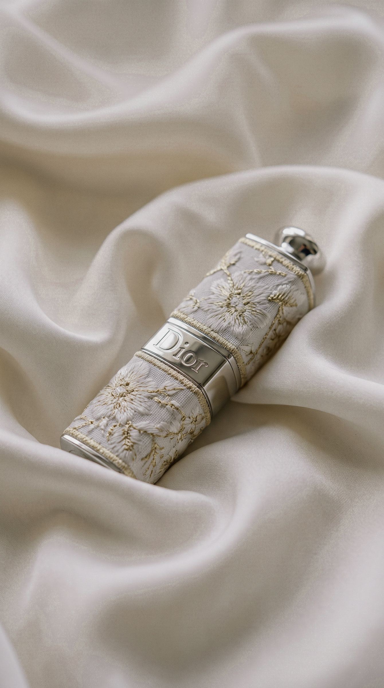 Un labial de Dior con estuche bordado, tumbado sobre seda blanca.