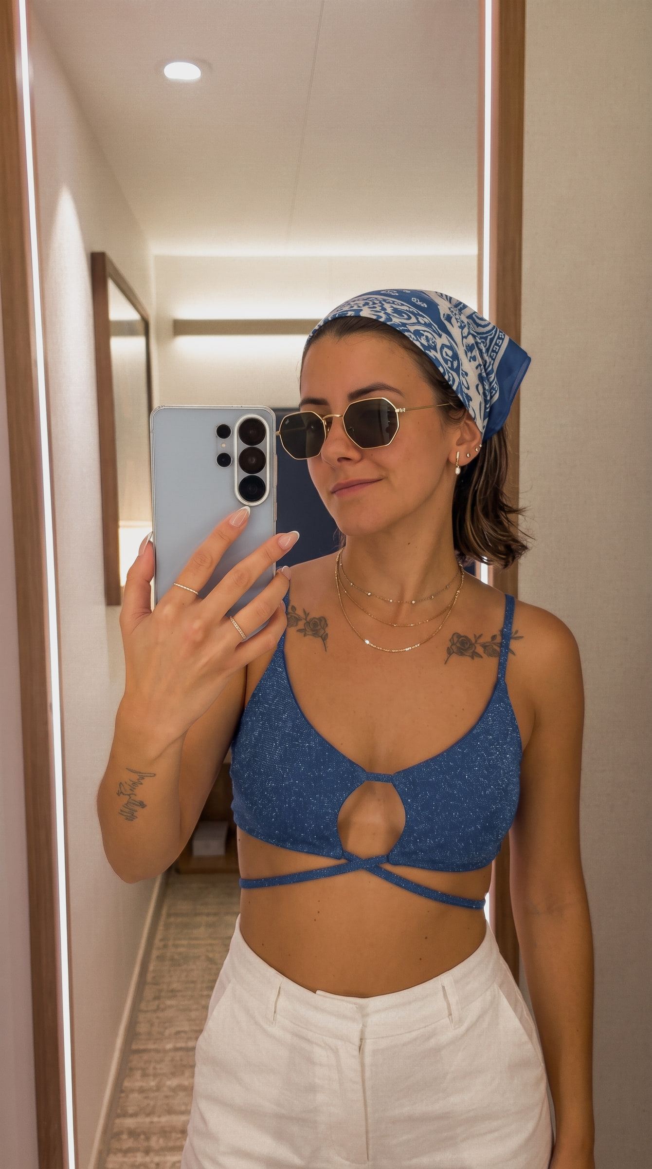IA. Selfie de probador con un conjunto de lino azul y, tras la edición con IA, la misma foto con top azul cruzado, pañuelo estampado y gafas de sol.