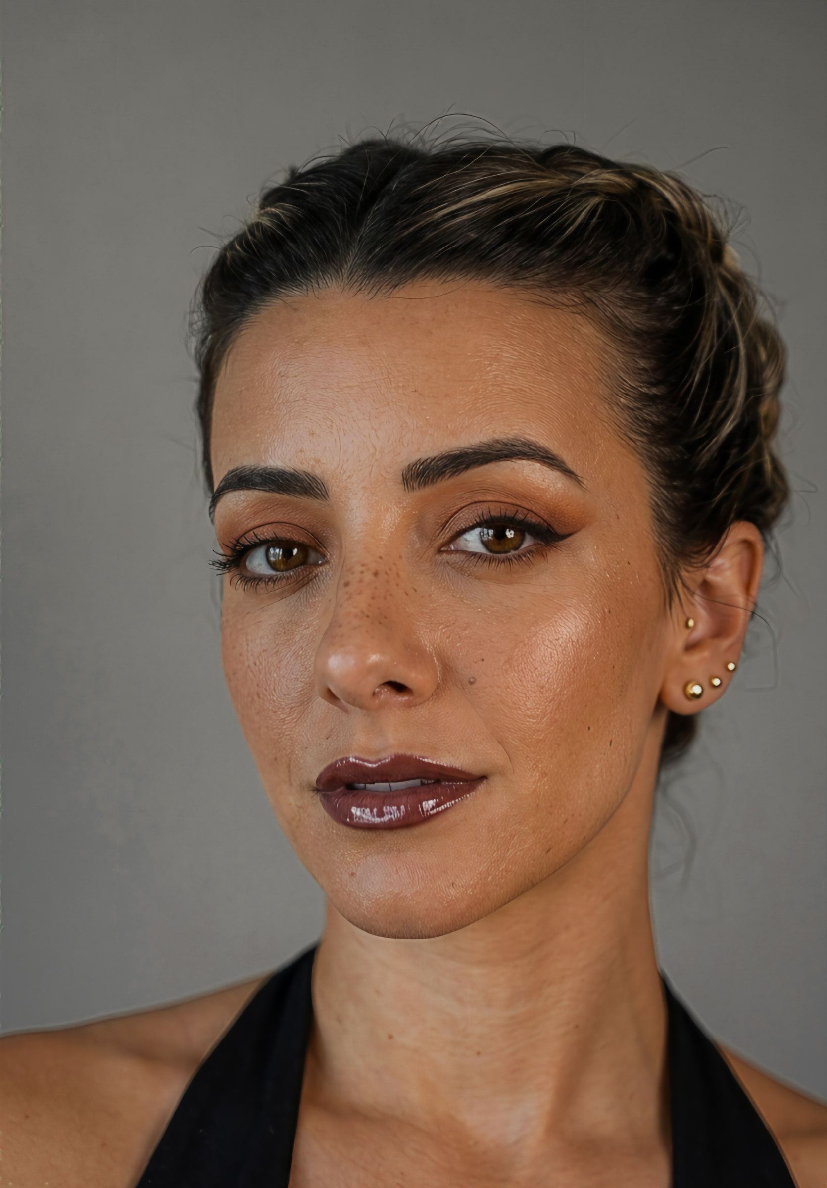Retrato sobre fondo gris con delineado fino, sombra cobre y labio ciruela de acabado vinilo.