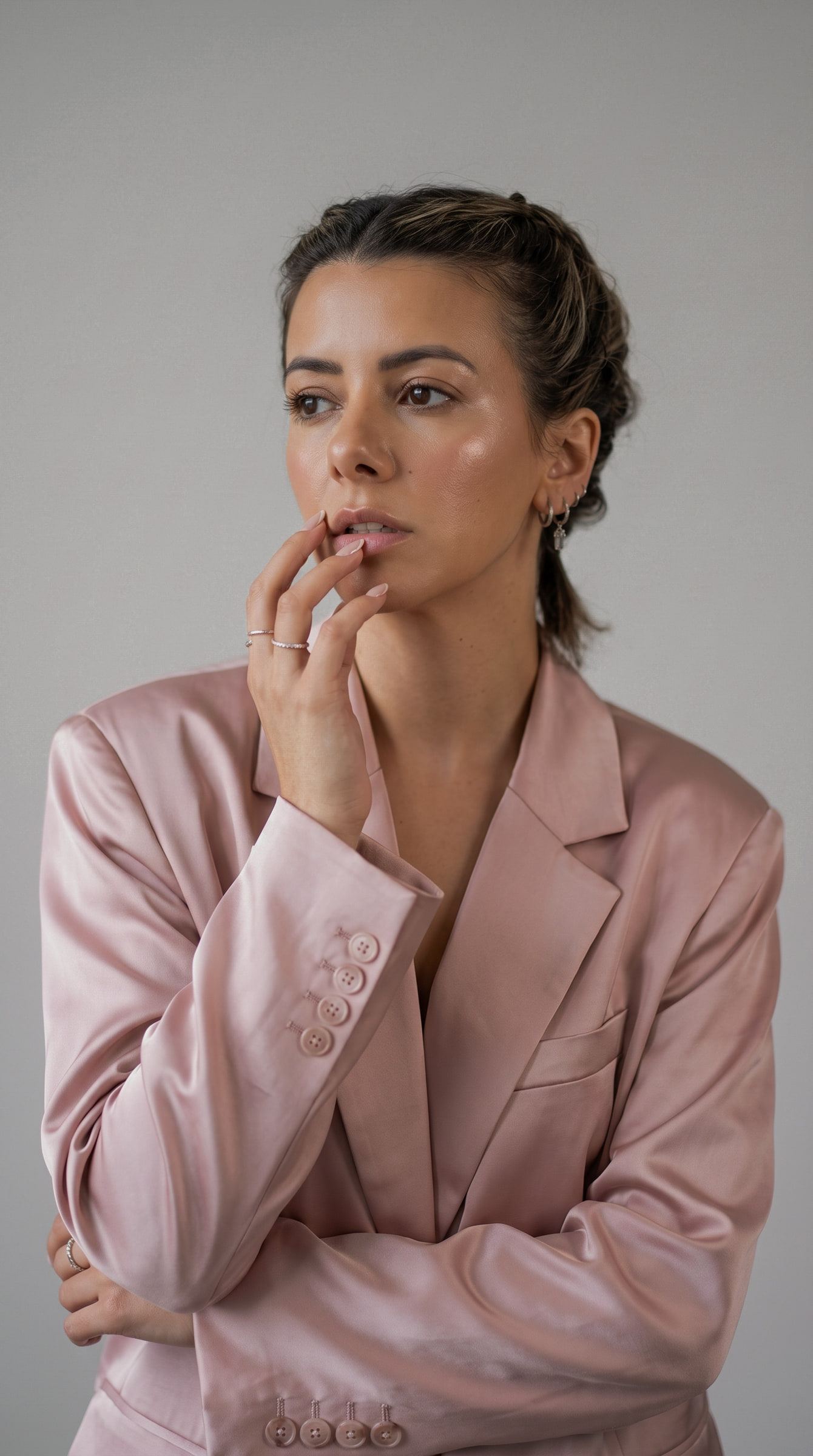 Retrato de estudio de Patricia Fenutria con blazer de satén rosa, la mano en la barbilla y la mirada fuera de cuadro