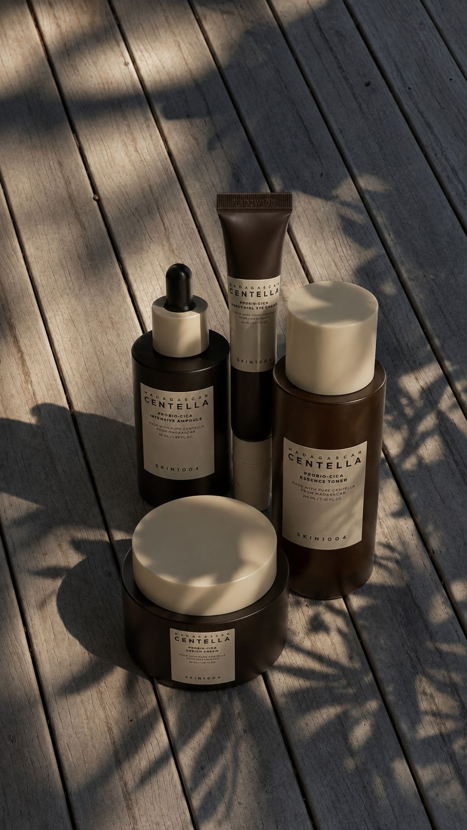 IA. Cuatro productos de cuidado facial recortados sobre blanco y, generado con IA, el mismo conjunto agrupado sobre una tarima de madera con sombras de hojas.